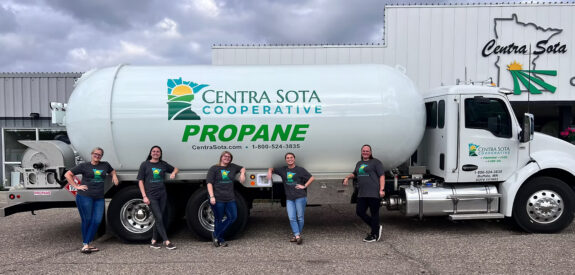 Five women in matching shirts smile together in front of a Centra Sota Cooperative propane truck.