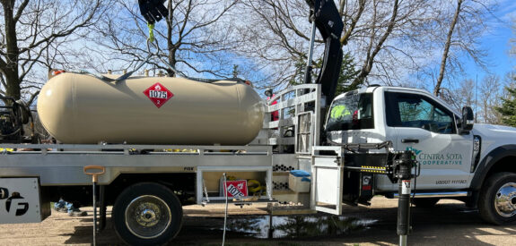 White Centra Sota Cooperative truck with propane tank labeled hazardous material 1075 in a rural setting.