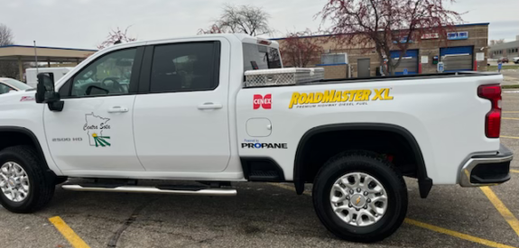White pickup truck bearing RoadMaster XL and PROFANE decals, parked by stores on a cloudy day.
