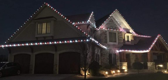 House at night with white and red holiday lights outlining the roof and garage.