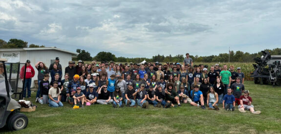 A large group stands on a lawn beneath a cloudy sky beside a white building.