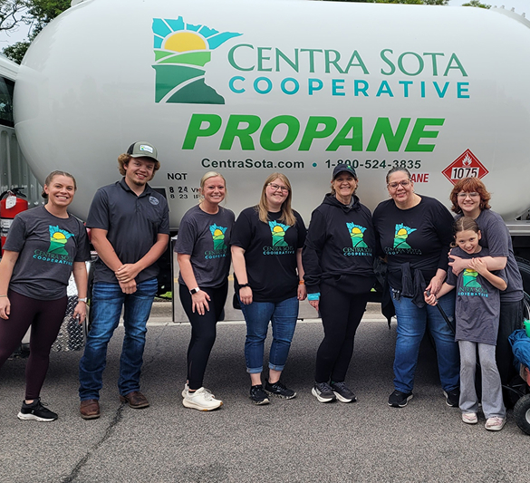 Seven smiling people in Centra Sota Cooperative shirts stand together in front of a large propane tank.
