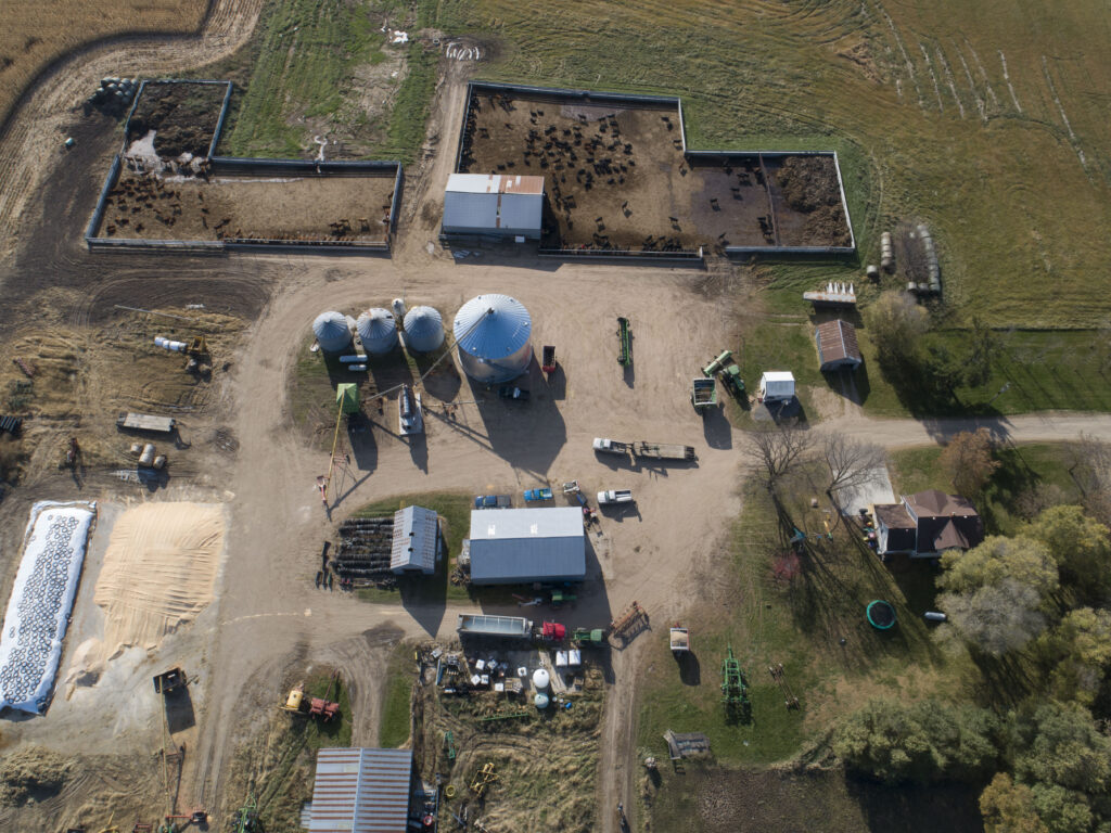 Aerial view of a grassy farm with silos, barns, equipment, and fenced pens for livestock.