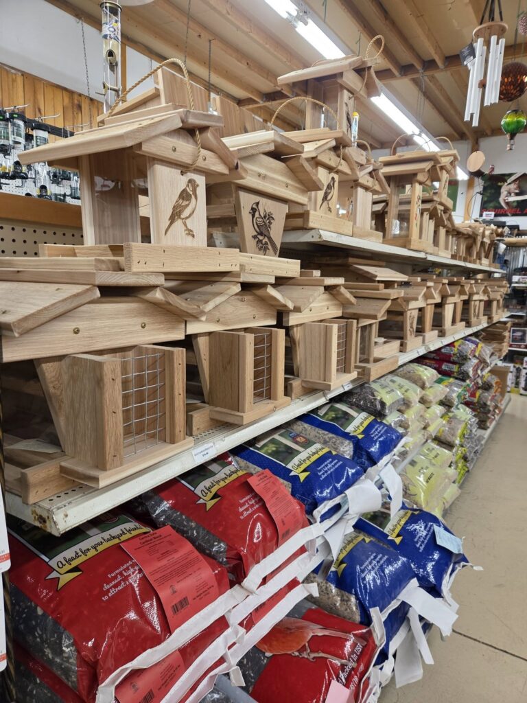 Bird feeders displayed on shelves above large bags of bird seed at a garden supply store.