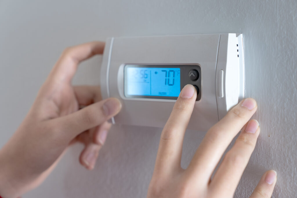 Fingers turning a wall-mounted digital thermostat set to 70 degrees.
