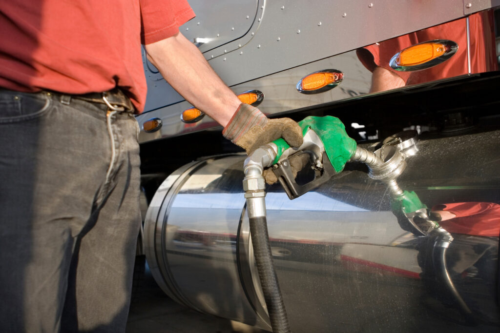 Someone fills up a big truck at a gas station using a green diesel nozzle.