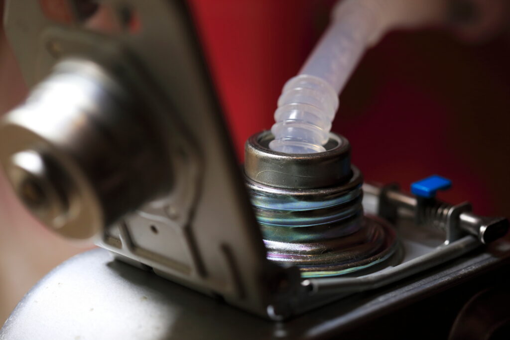 Plastic tube inserted into a metal container’s opening, suggesting a liquid transfer process, shown in close-up.