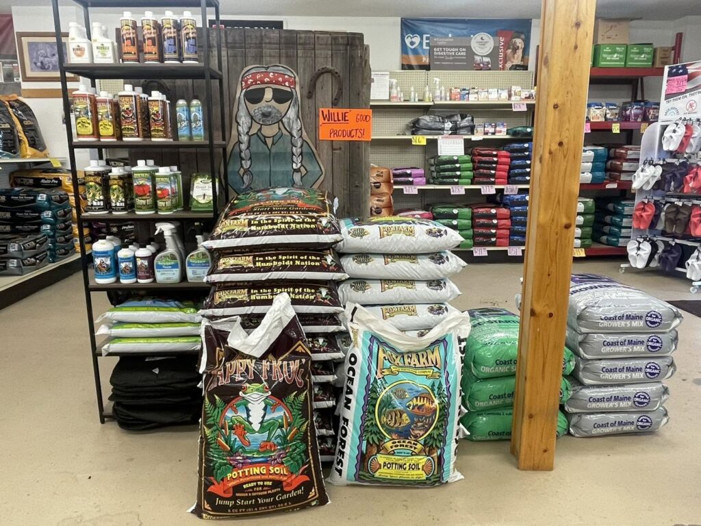 Potting soil bags and gardening products stacked on store shelves beside a wooden post.
