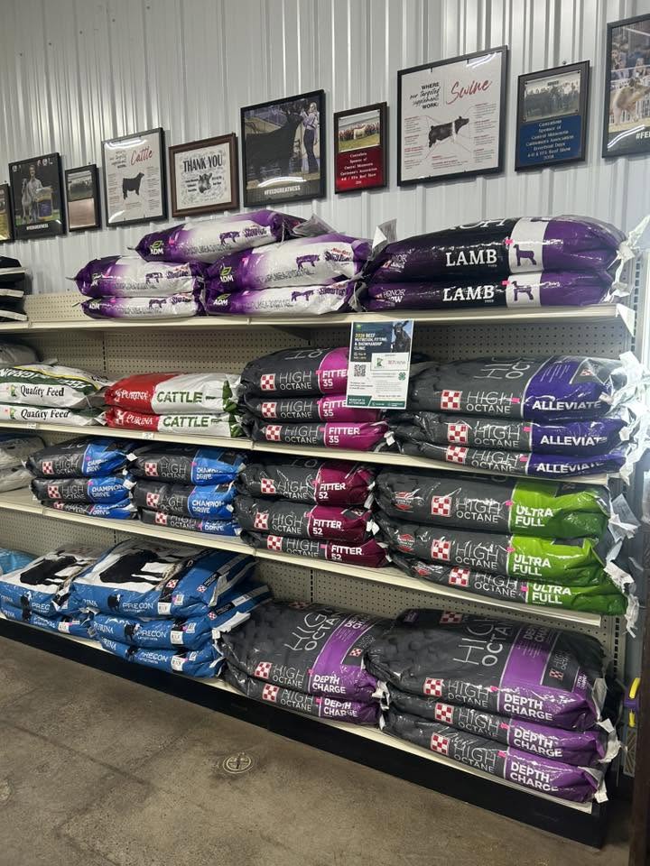 Animal feed bags stacked on metal shelves below framed awards hanging on a store wall.