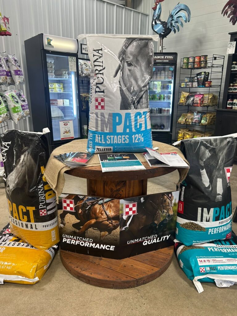 Purina horse feed bags stacked on and near a wooden spool table inside a store.