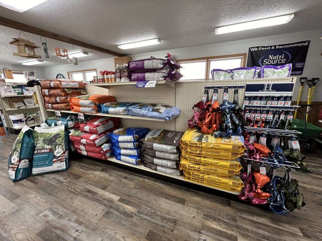Pet food bags and supplies on store shelves; leashes and accessories arranged to the right.