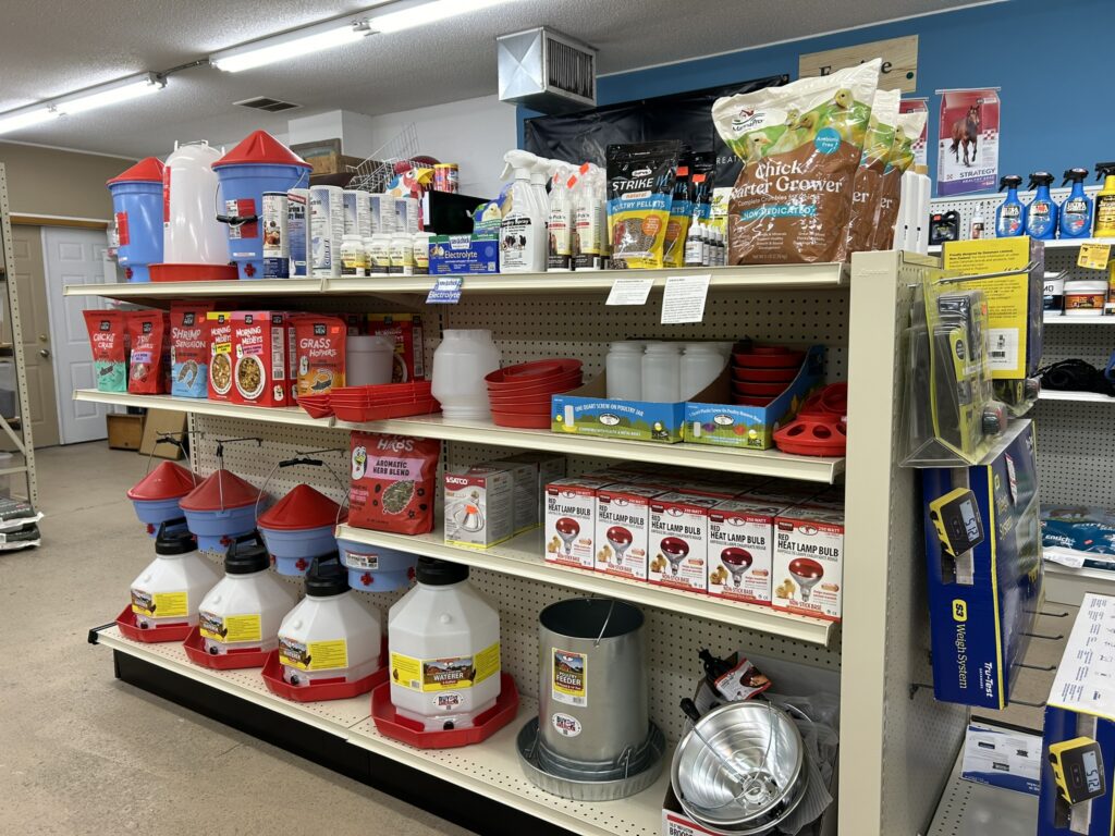 Store shelves filled with poultry supplies, feeders, waterers, feed bags, and cleaning products.
