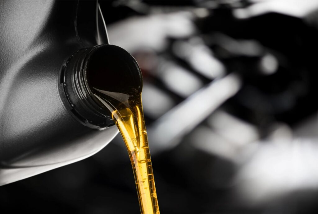 Golden motor oil flows from a black plastic container, background softly blurred for focus on the liquid.