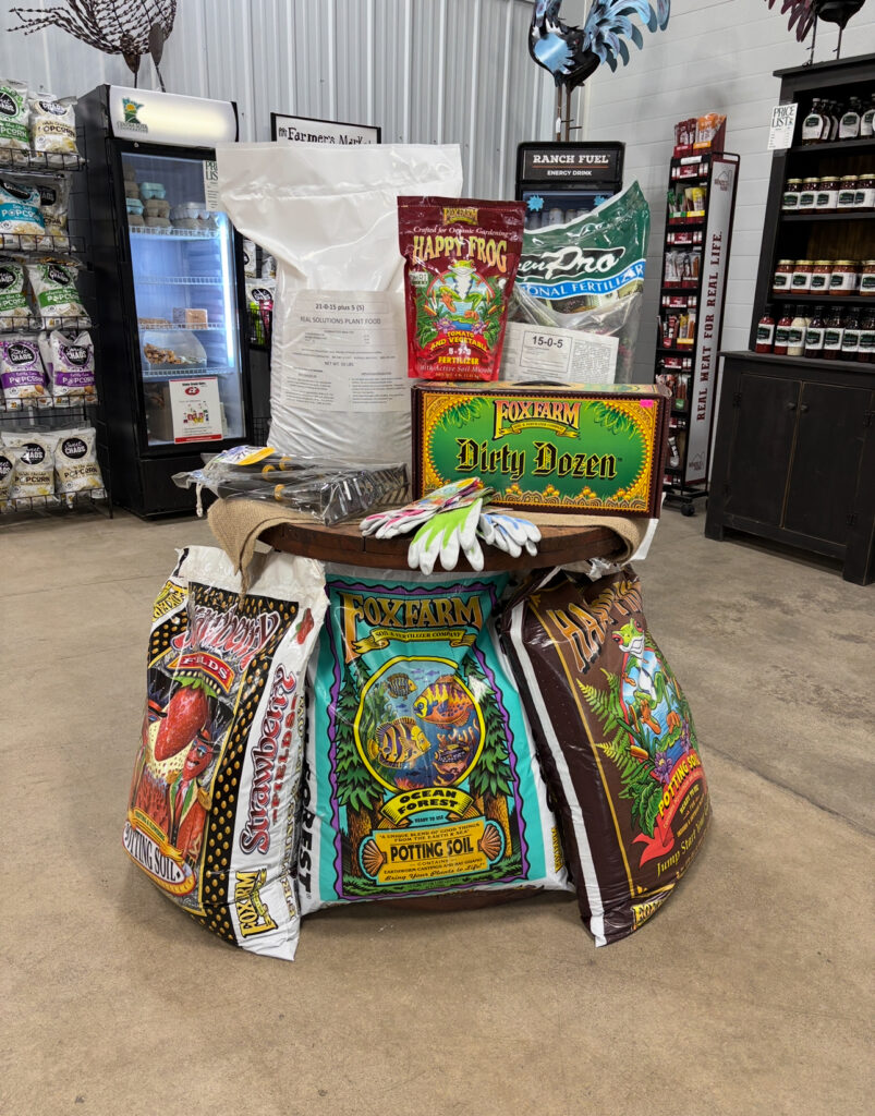 FoxFarm soil, plant food bags, gloves, and gardening supplies arranged on a round table in a store.